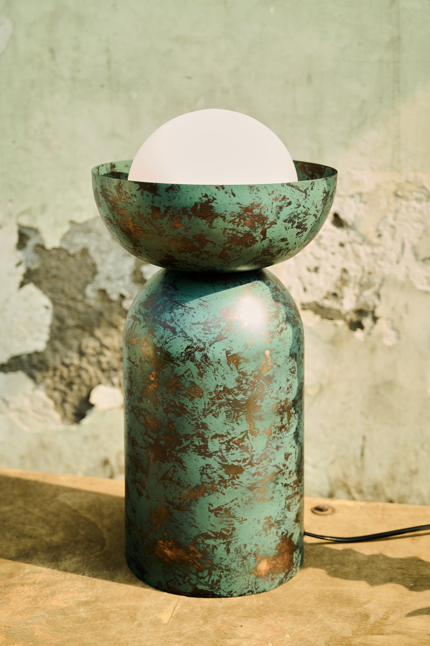 Vintage-style teal lamp with a white bulb against a textured wall.