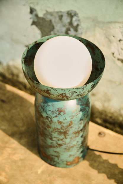 Rustic green metal vase with a white candle inside on a textured surface