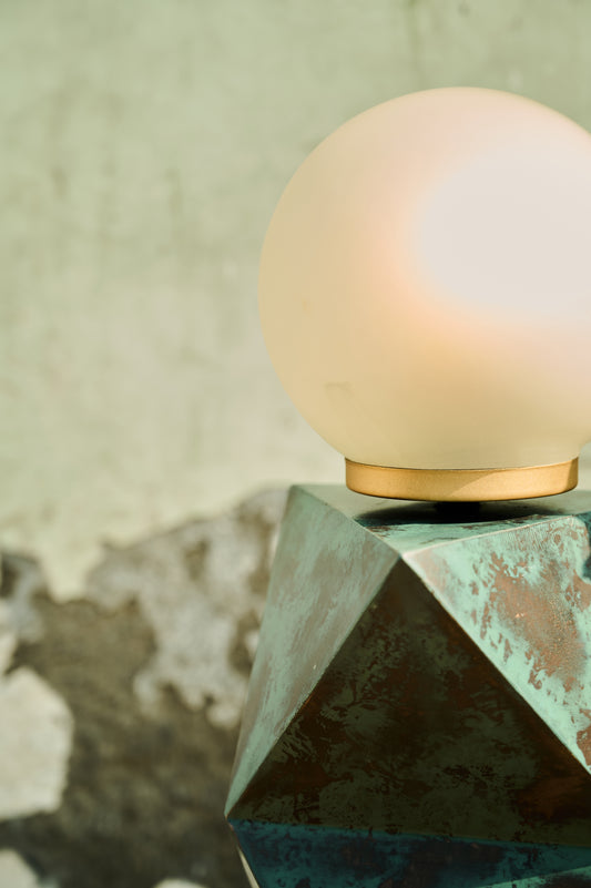 Decorative lamp with a geometric base and round glass shade on a textured surface.