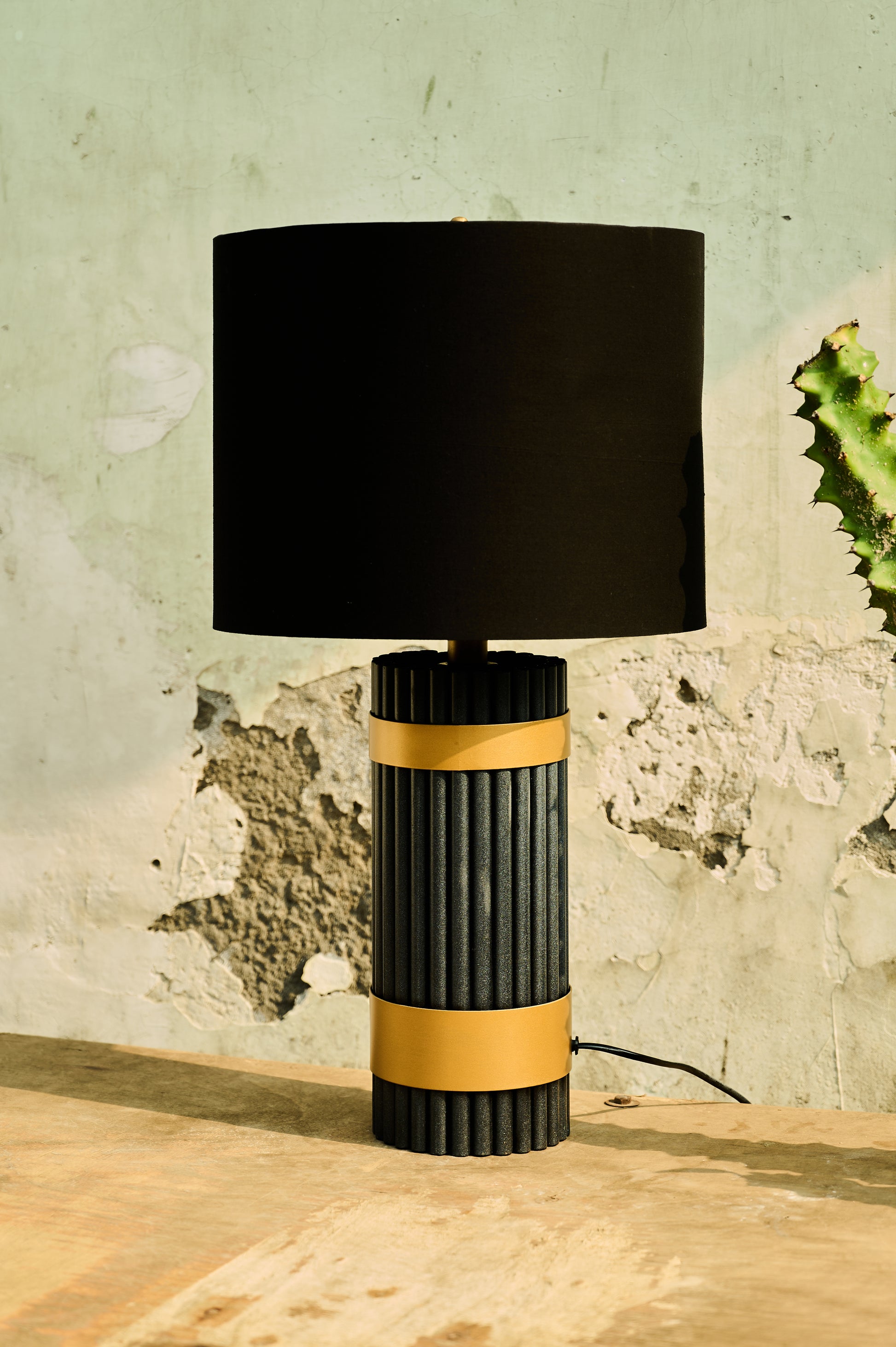 Table lamp with black and gold design on a wooden surface against a textured wall.