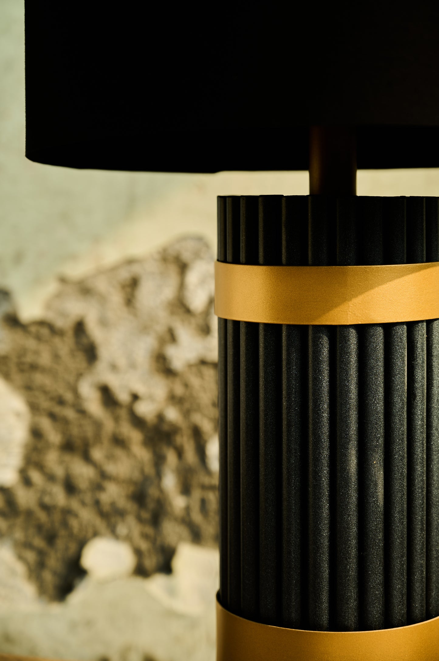 Black and gold lamp with textured design against a blurred natural background