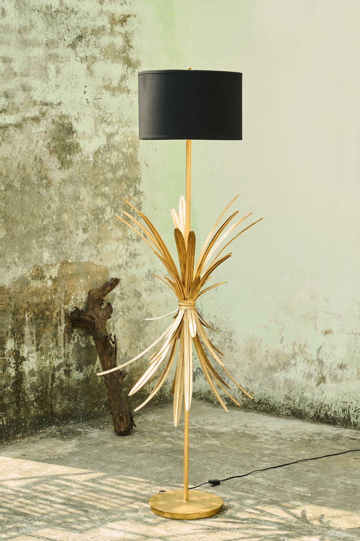 Decorative floor lamp with gold base and black shade against a textured wall.