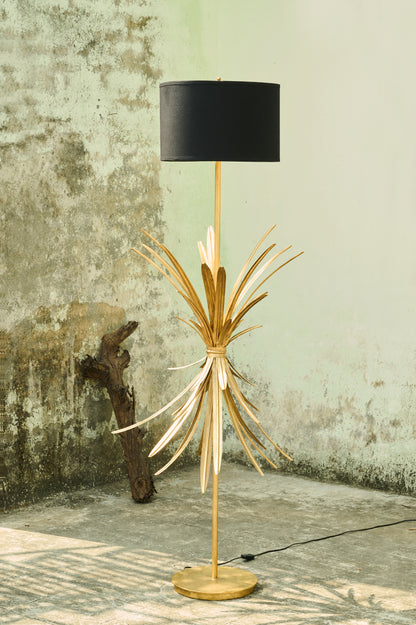 Decorative floor lamp with gold base and black shade against a textured wall.