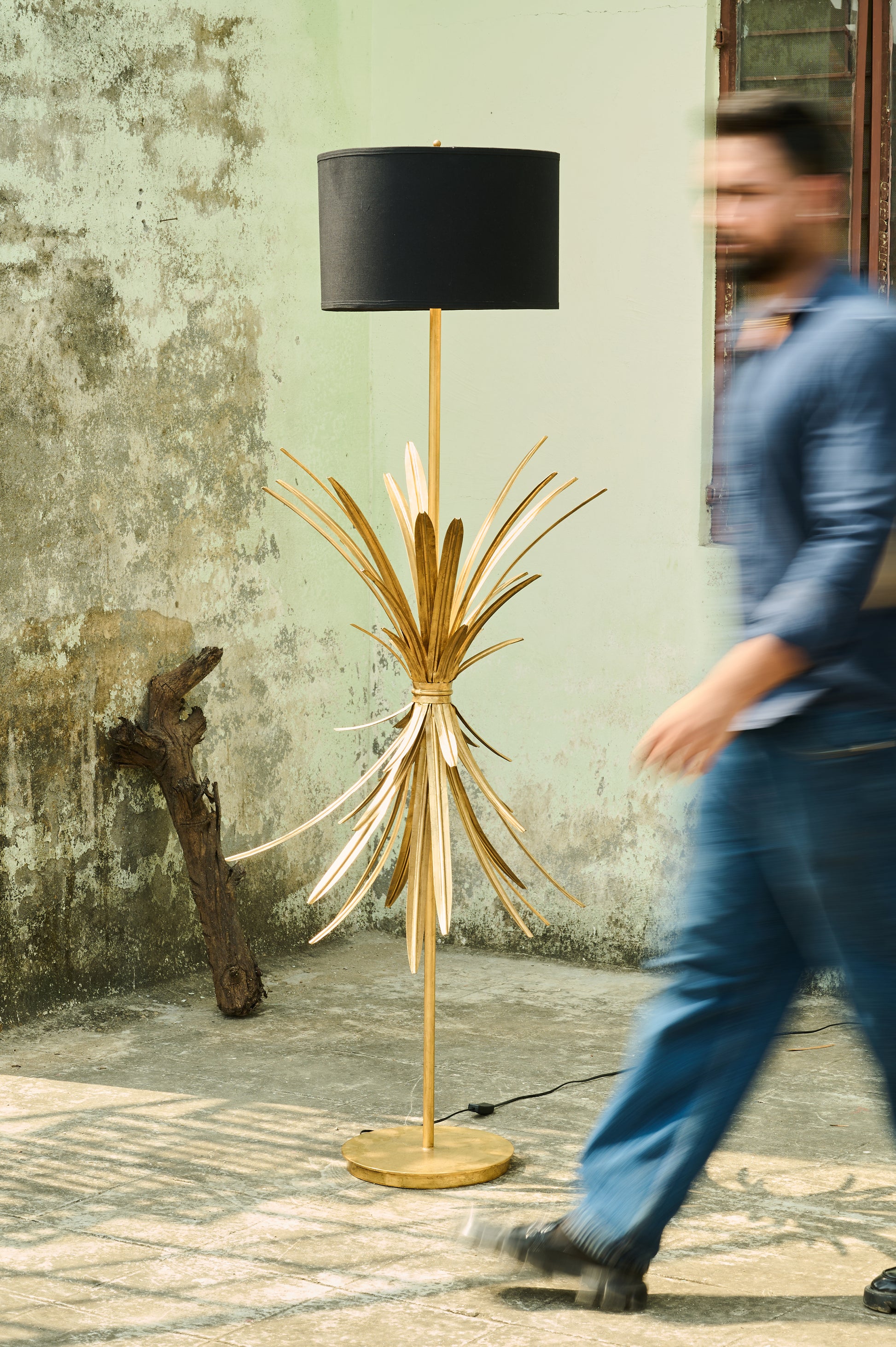 Floor lamp with a unique design next to a person walking by a textured wall.