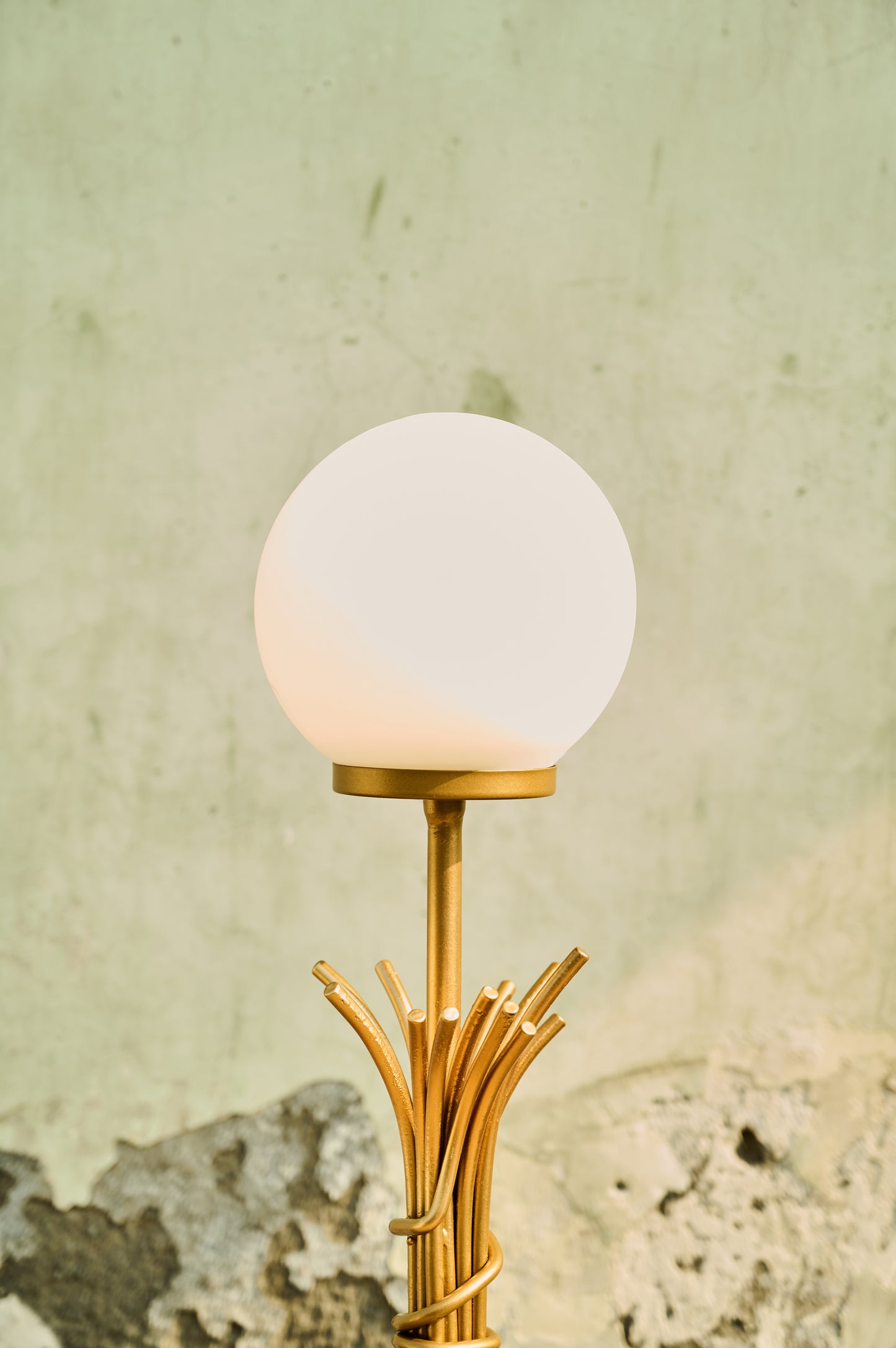 Decorative lamp with a gold base and white globe shade against a textured wall.
