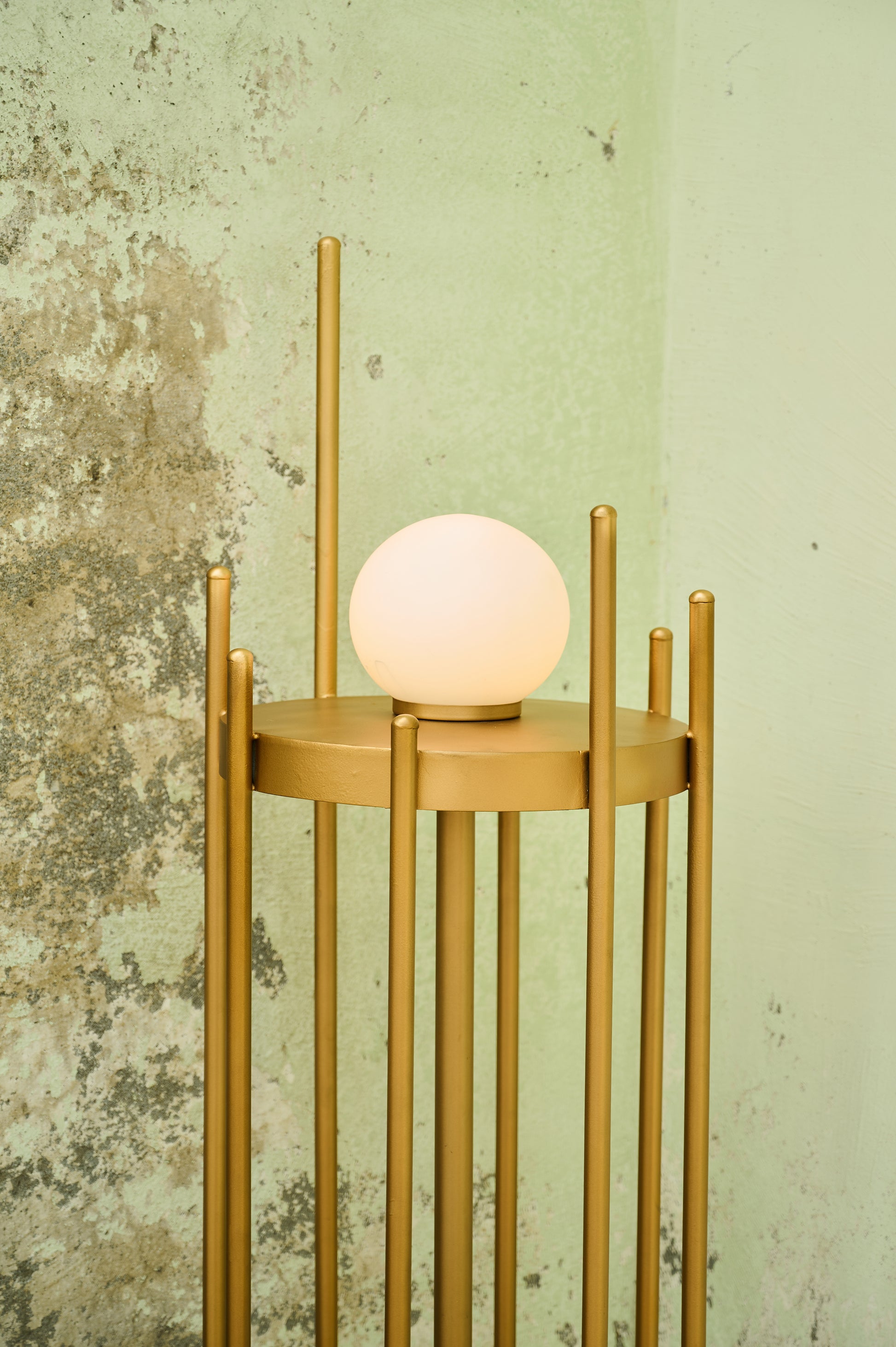 Gold floor lamp with a round white bulb against a textured wall.