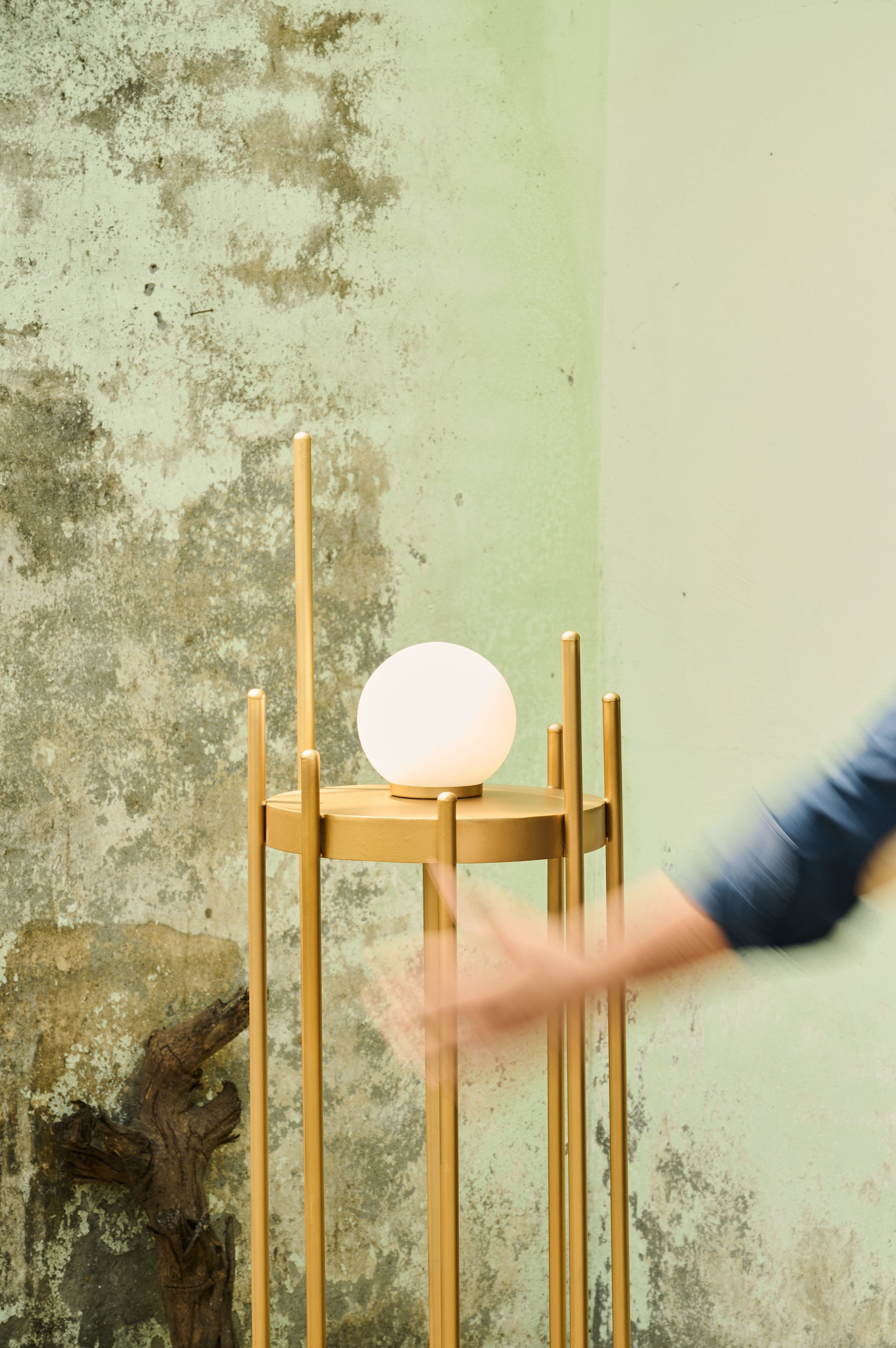 Gold floor lamp with a round white light bulb against a textured green wall.