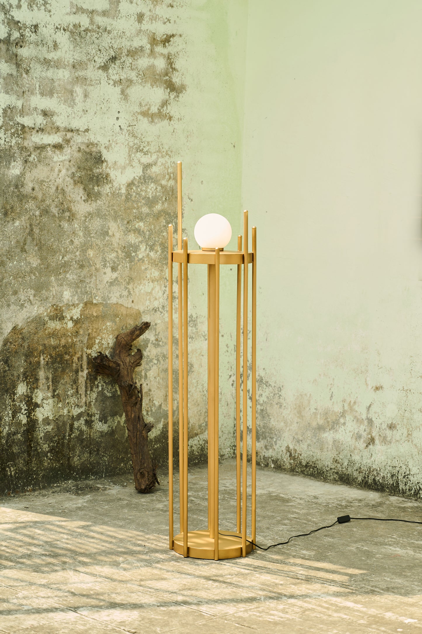 Wooden floor lamp with a spherical light bulb against a textured wall.