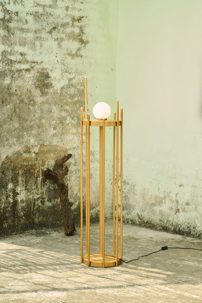 Wooden floor lamp with a spherical light bulb against a textured wall.