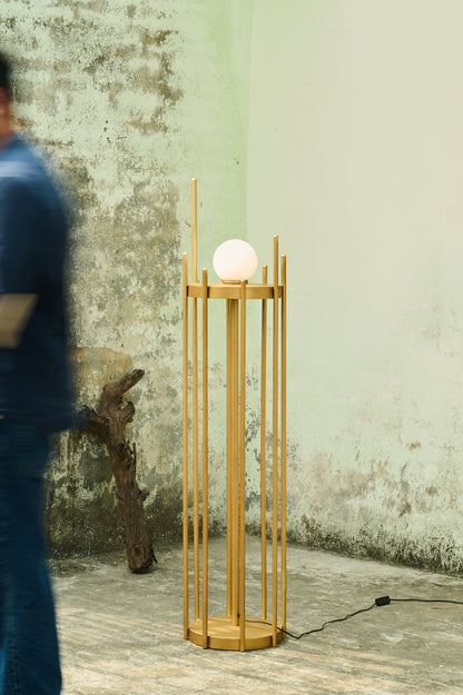 Wooden floor lamp with a spherical light bulb against a textured wall.