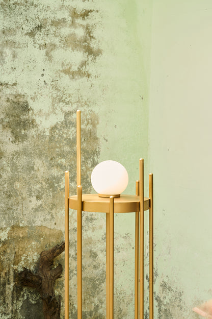 Gold floor lamp with a white spherical light bulb against a textured green wall.