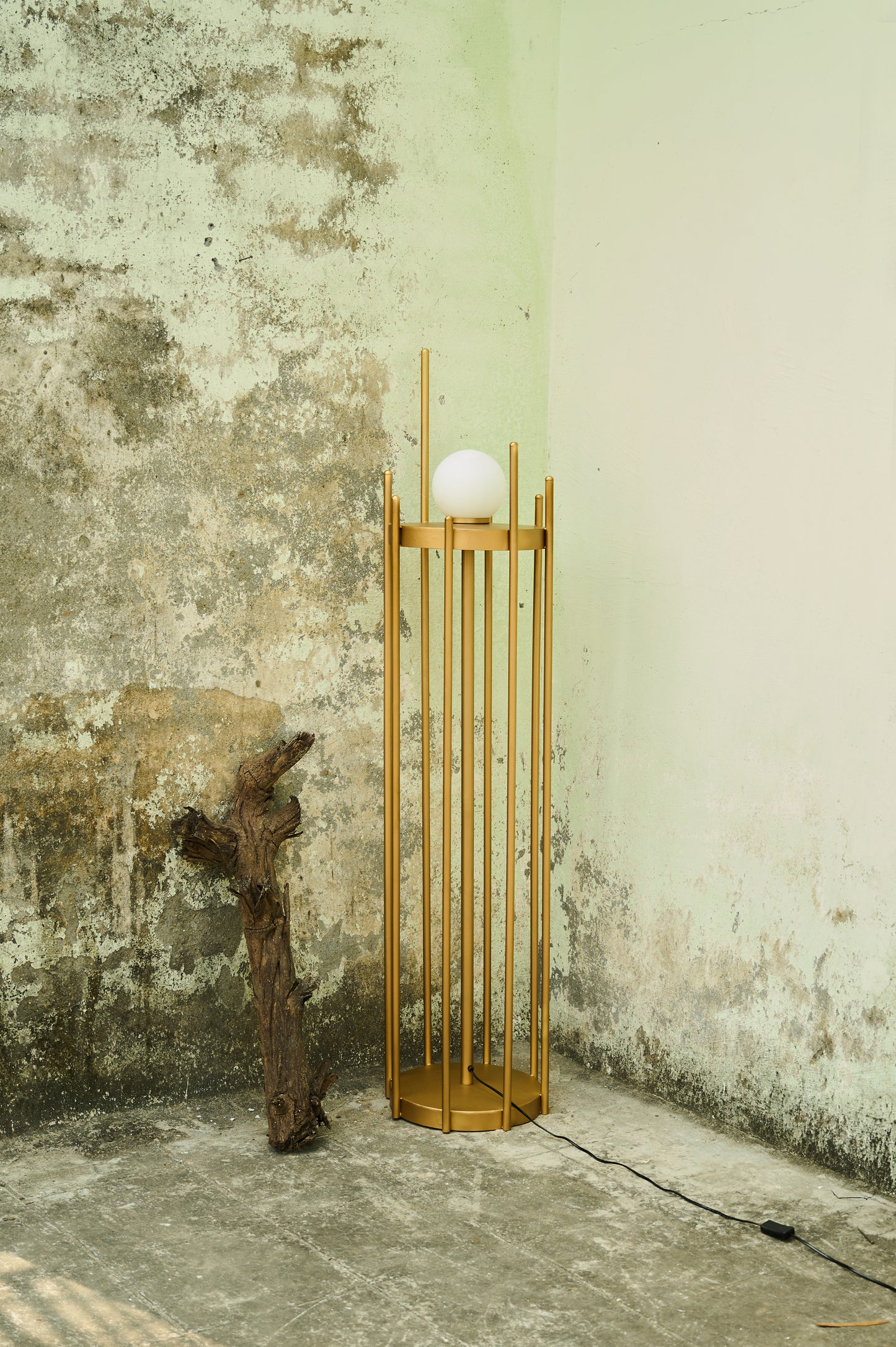 Wooden floor lamp with a spherical light bulb against a textured wall.