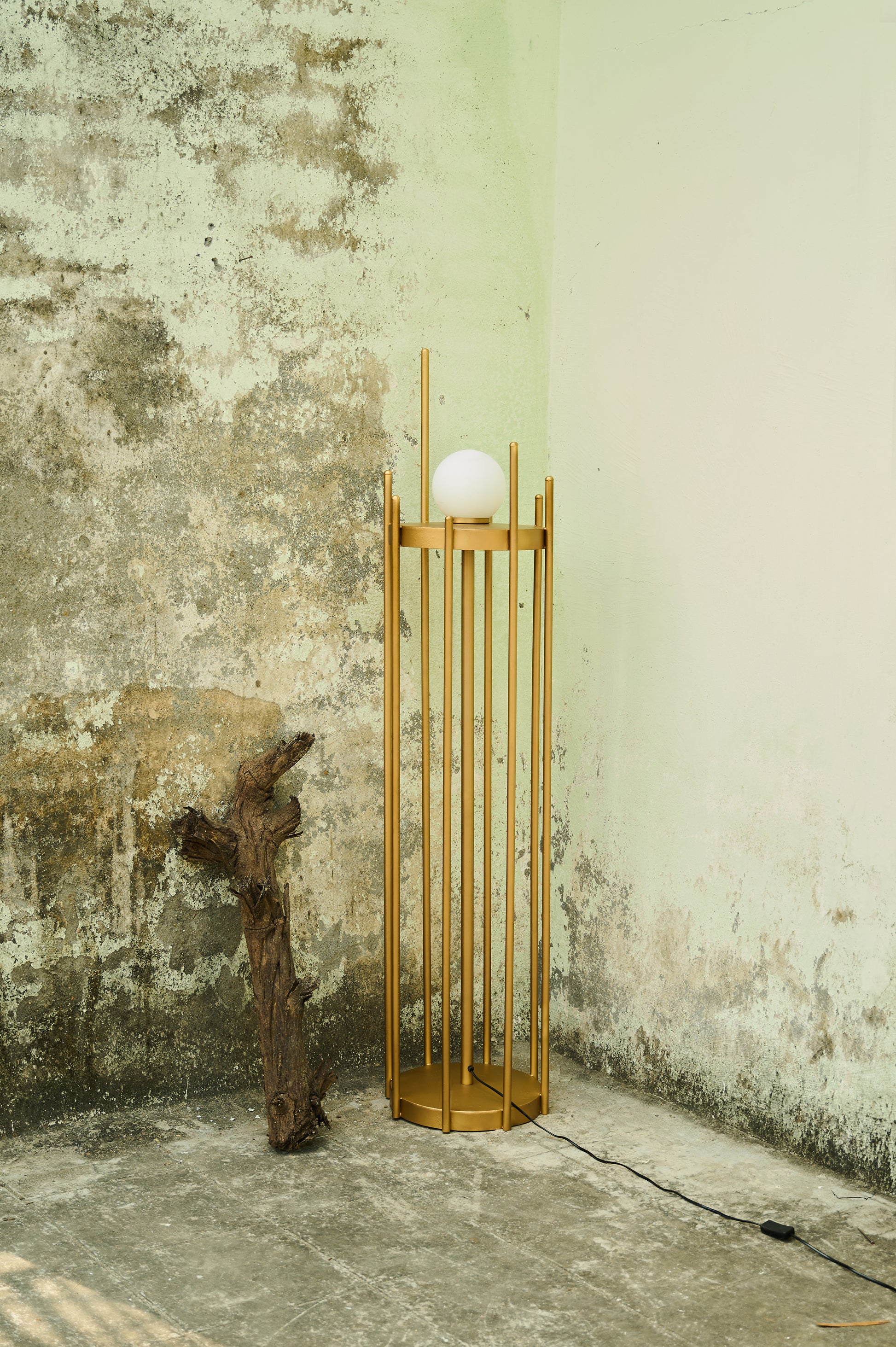 Wooden floor lamp with a spherical light bulb against a textured wall.