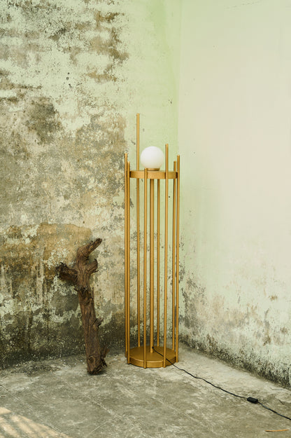 Wooden floor lamp with a spherical light bulb against a textured wall.