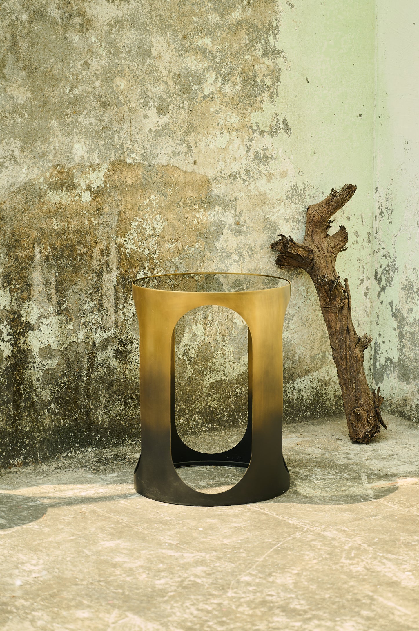 Bronze candle holder against a textured wall with a branch
