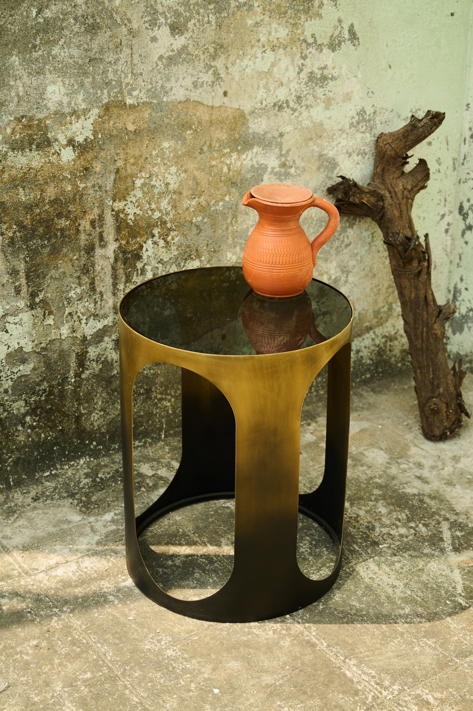 Small round table with a textured surface on a stone floor against a rustic wall.