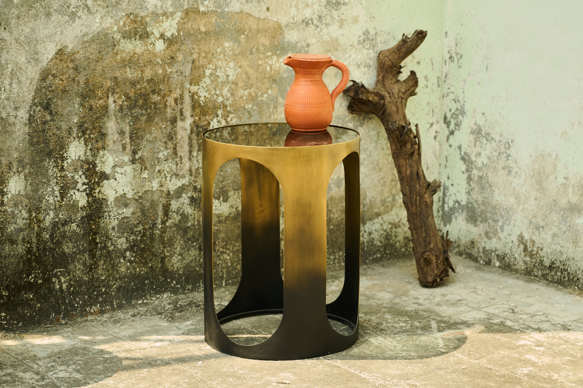 Bronze side table with a red ceramic pitcher on a textured wall background