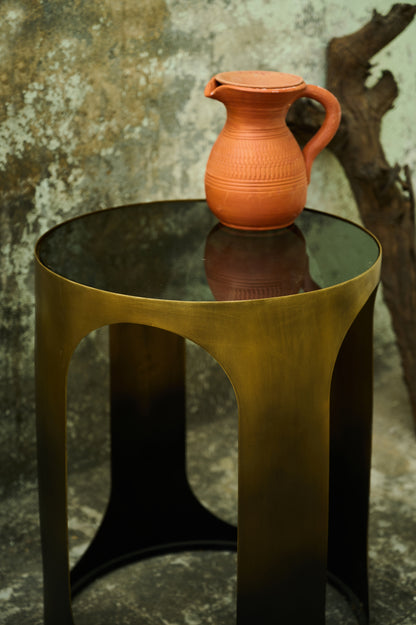 Terracotta pitcher on a black glass table against a textured wall.