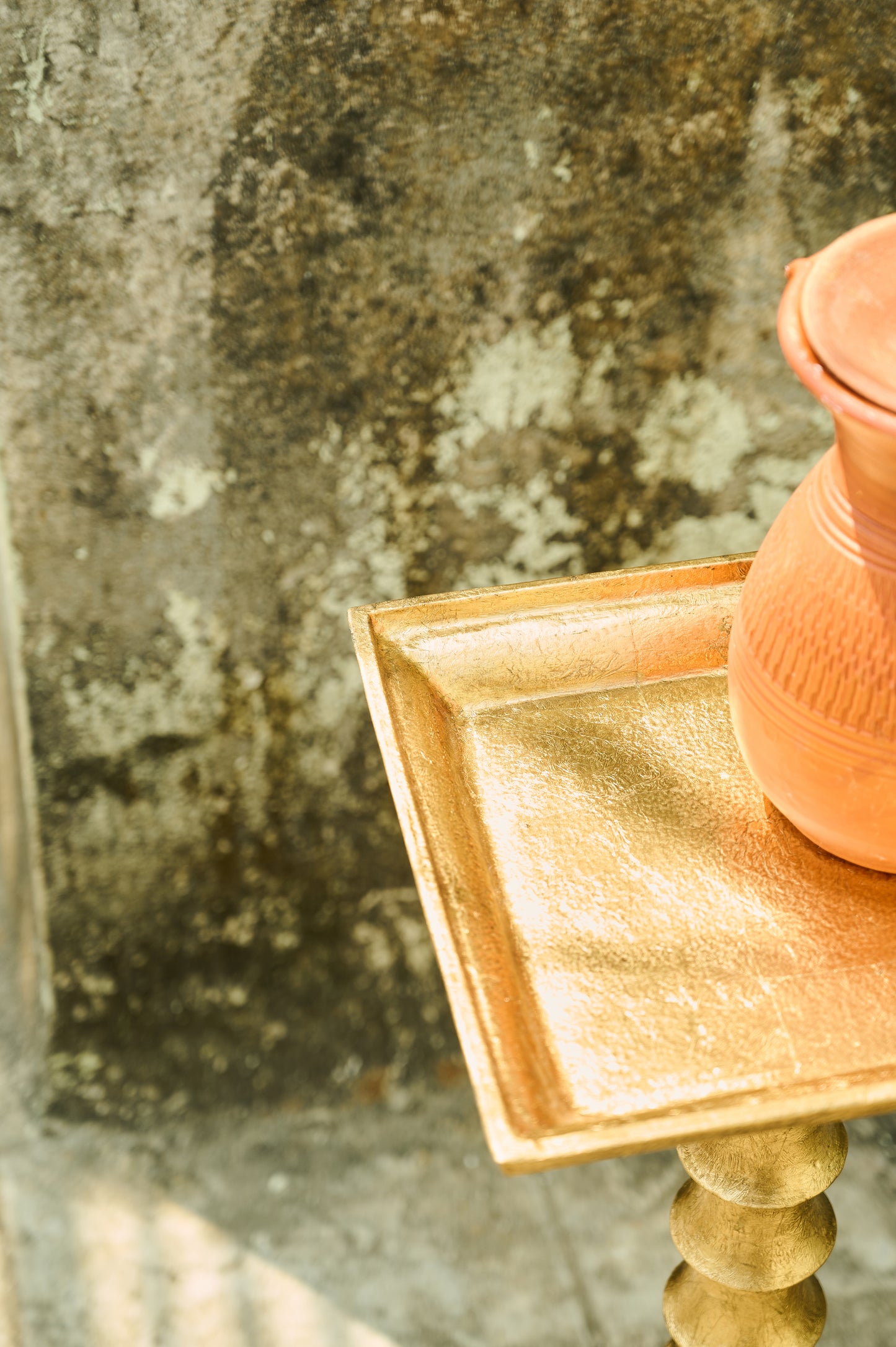 Pink ceramic vase on a gold stand with a textured stone background