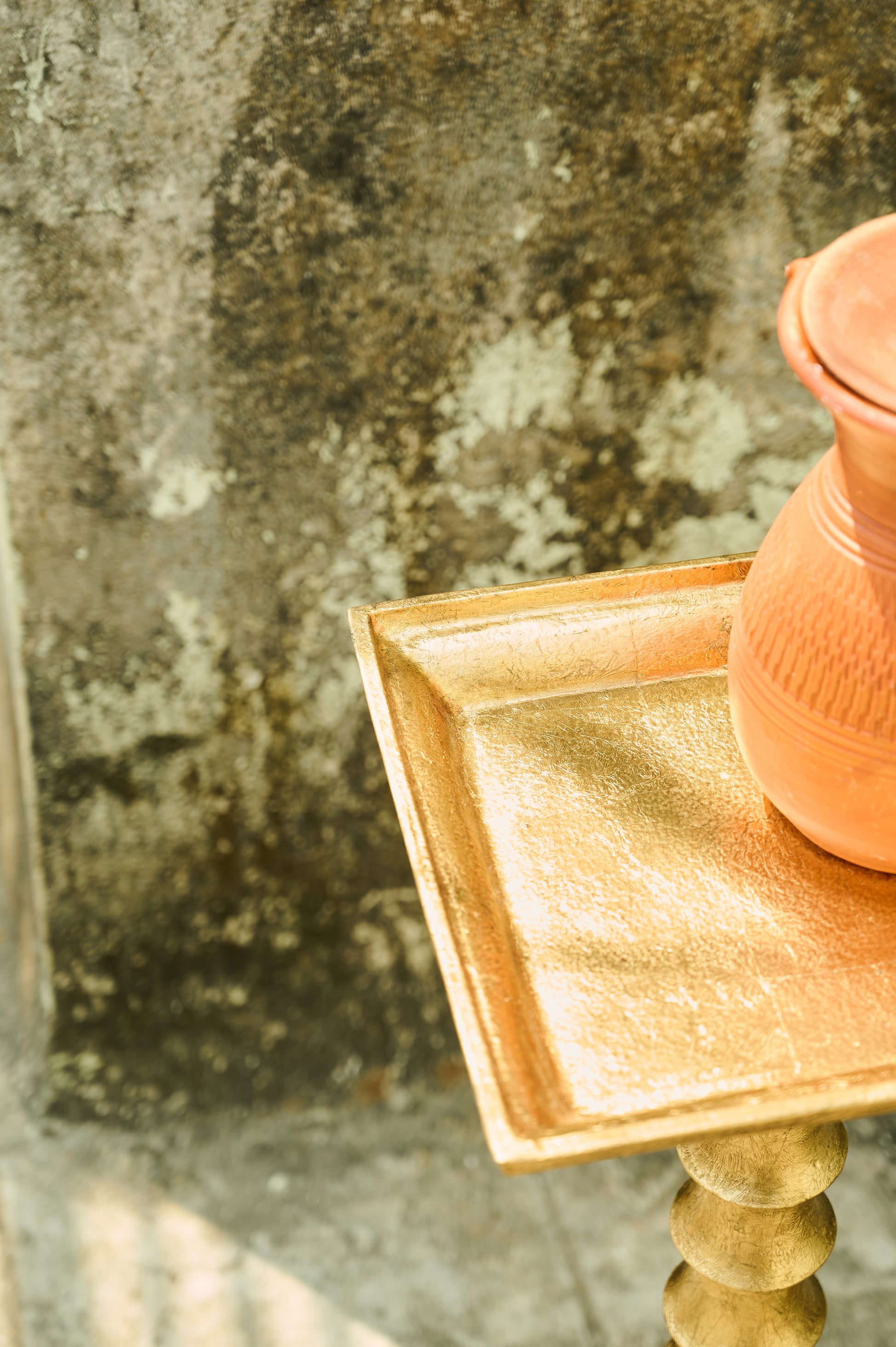 Pink ceramic vase on a gold stand with a textured stone background