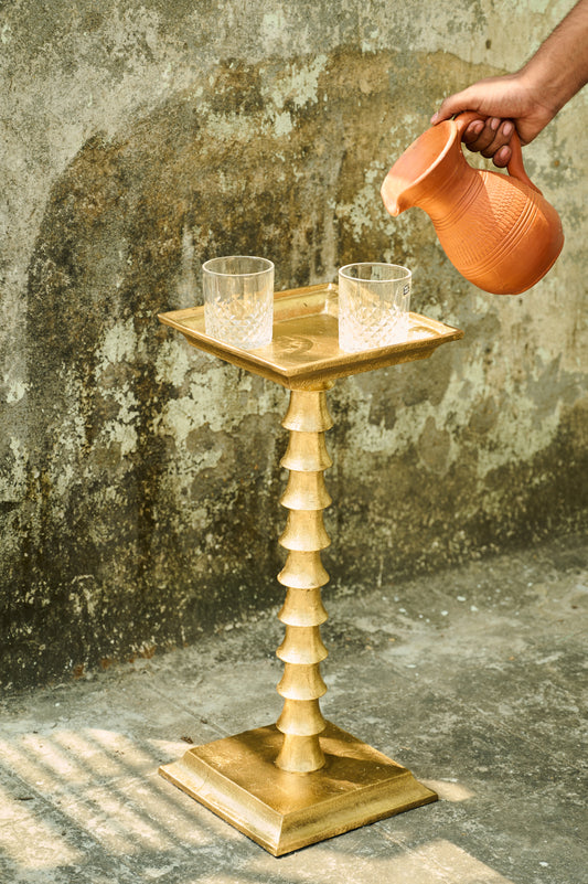 Gold side table with two glasses on a textured wall background