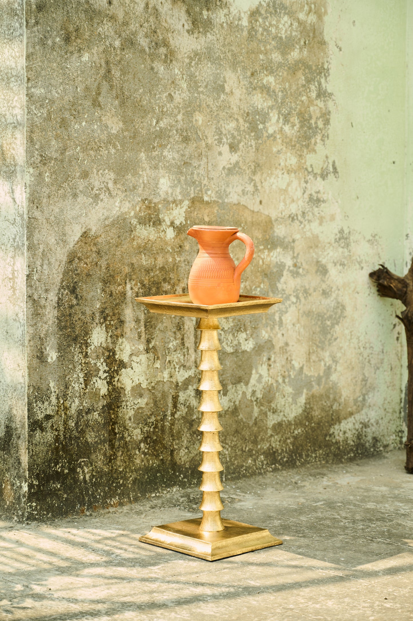 Terracotta pitcher on a wooden stand against a textured wall.