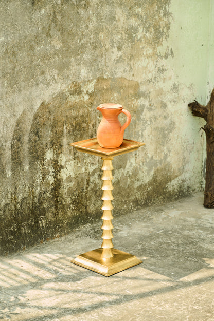 Terracotta pitcher on a wooden stand against a textured wall.