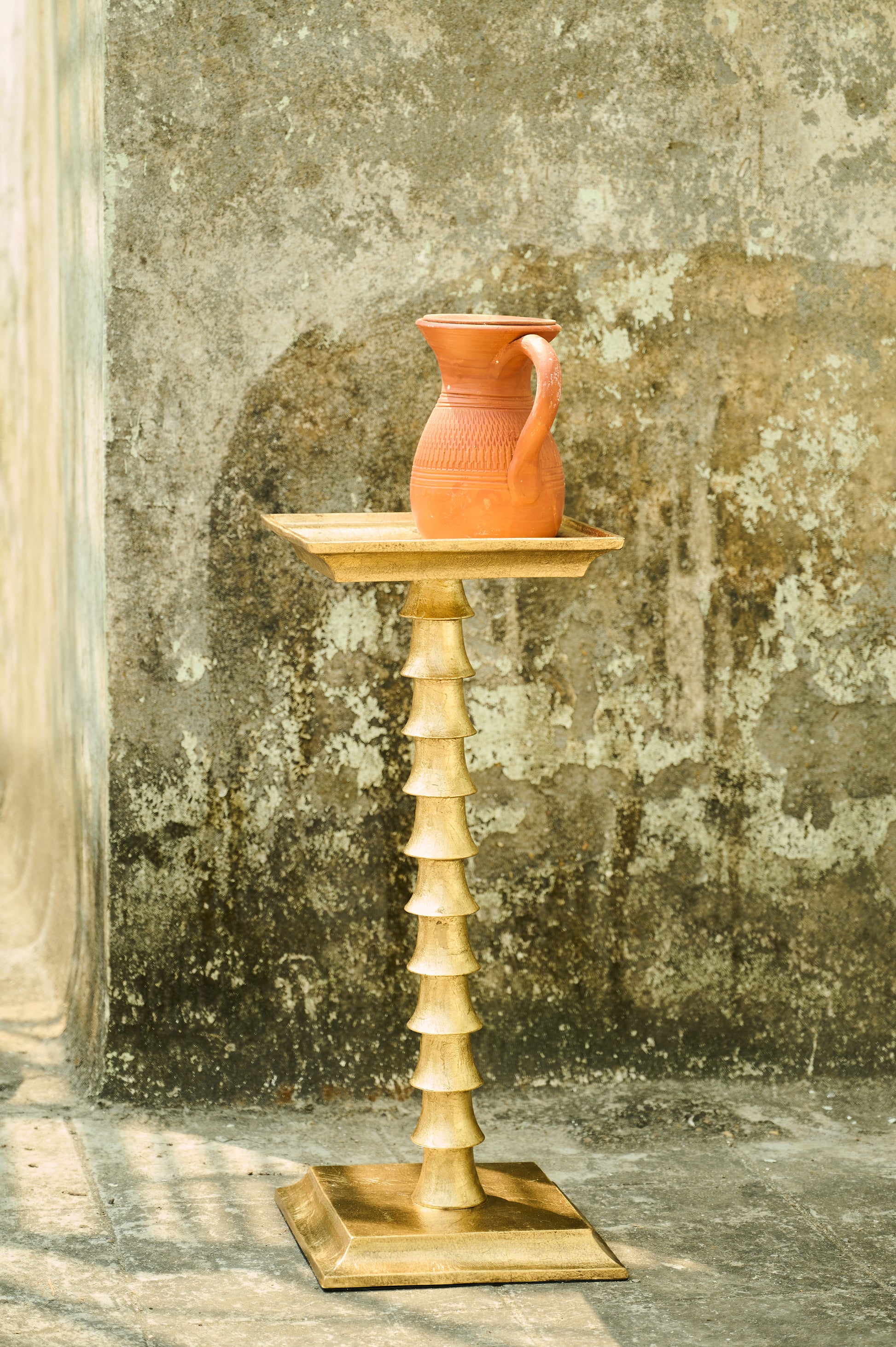 Terracotta pitcher on a wooden stand against a textured wall.