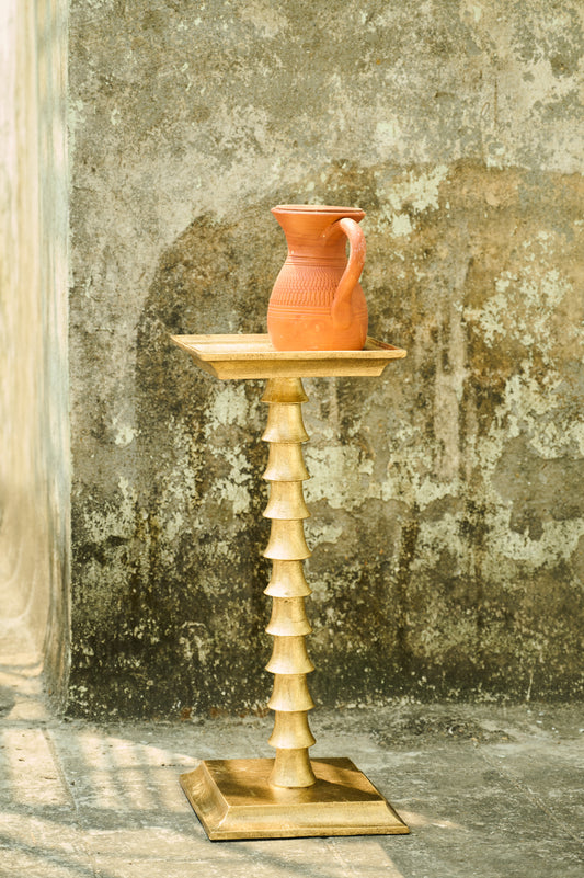 Terracotta pitcher on a wooden stand against a textured wall.
