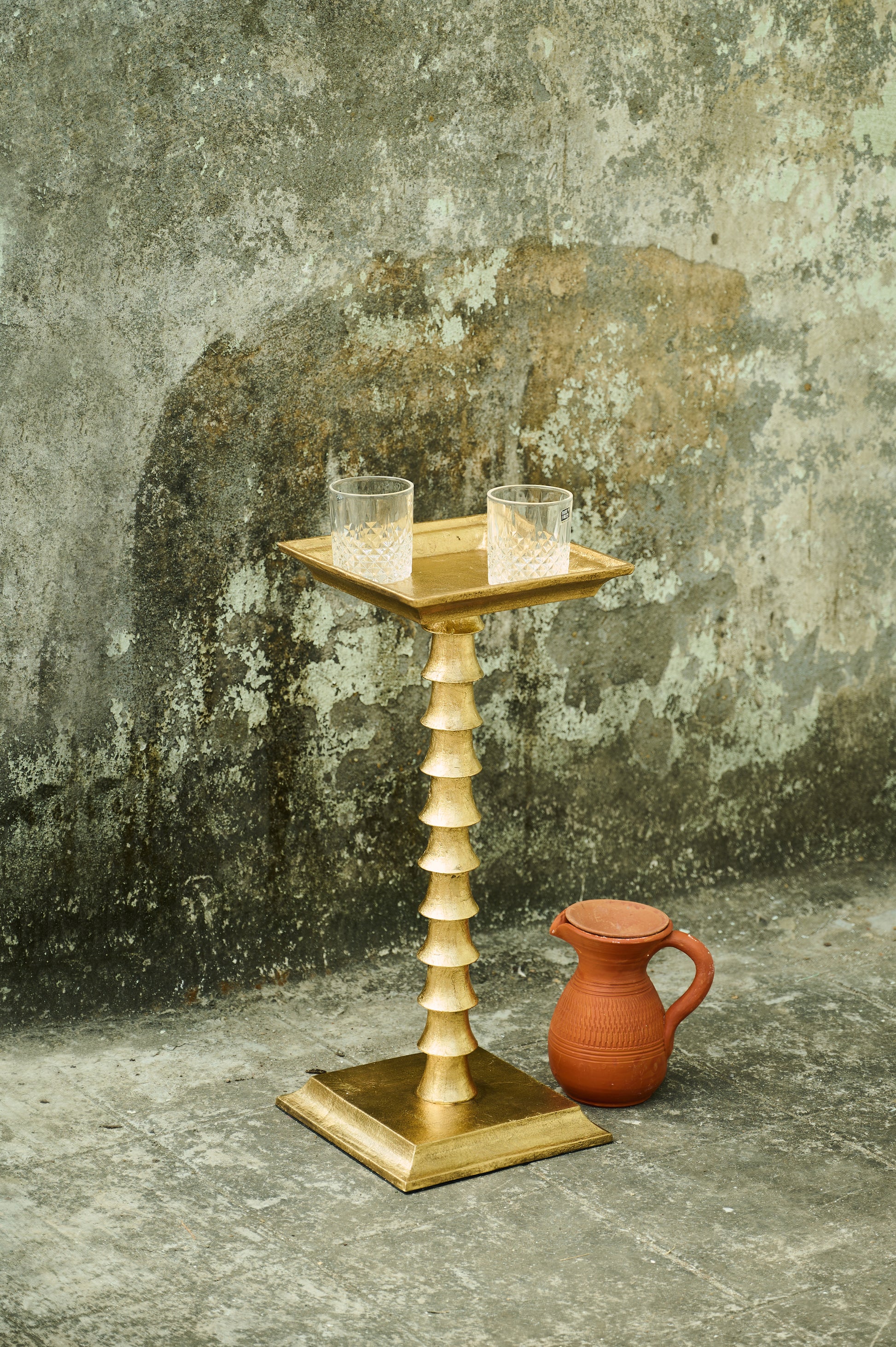 Wooden candle holder with two candles on a textured surface next to a terracotta pot.