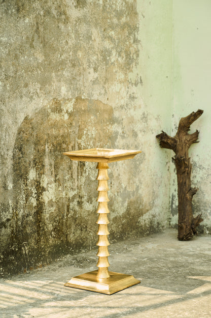 Gold pedestal table against a textured wall with a piece of driftwood.