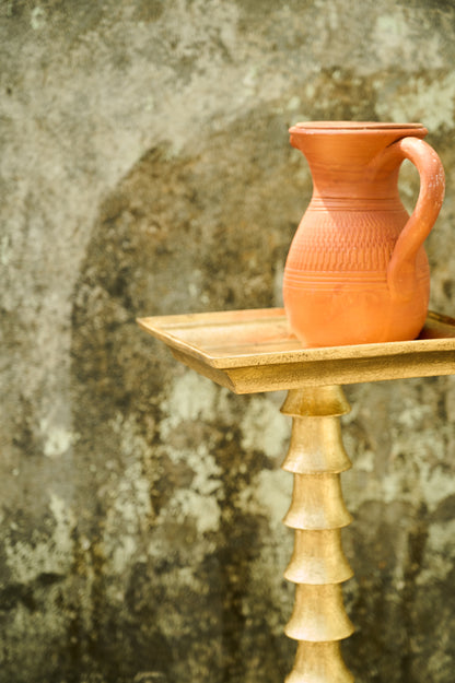 Terracotta pitcher on a wooden stand against a textured wall.
