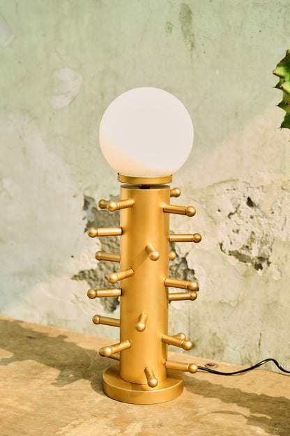 Gold table lamp with a round base and spherical glass shade on a wooden surface.