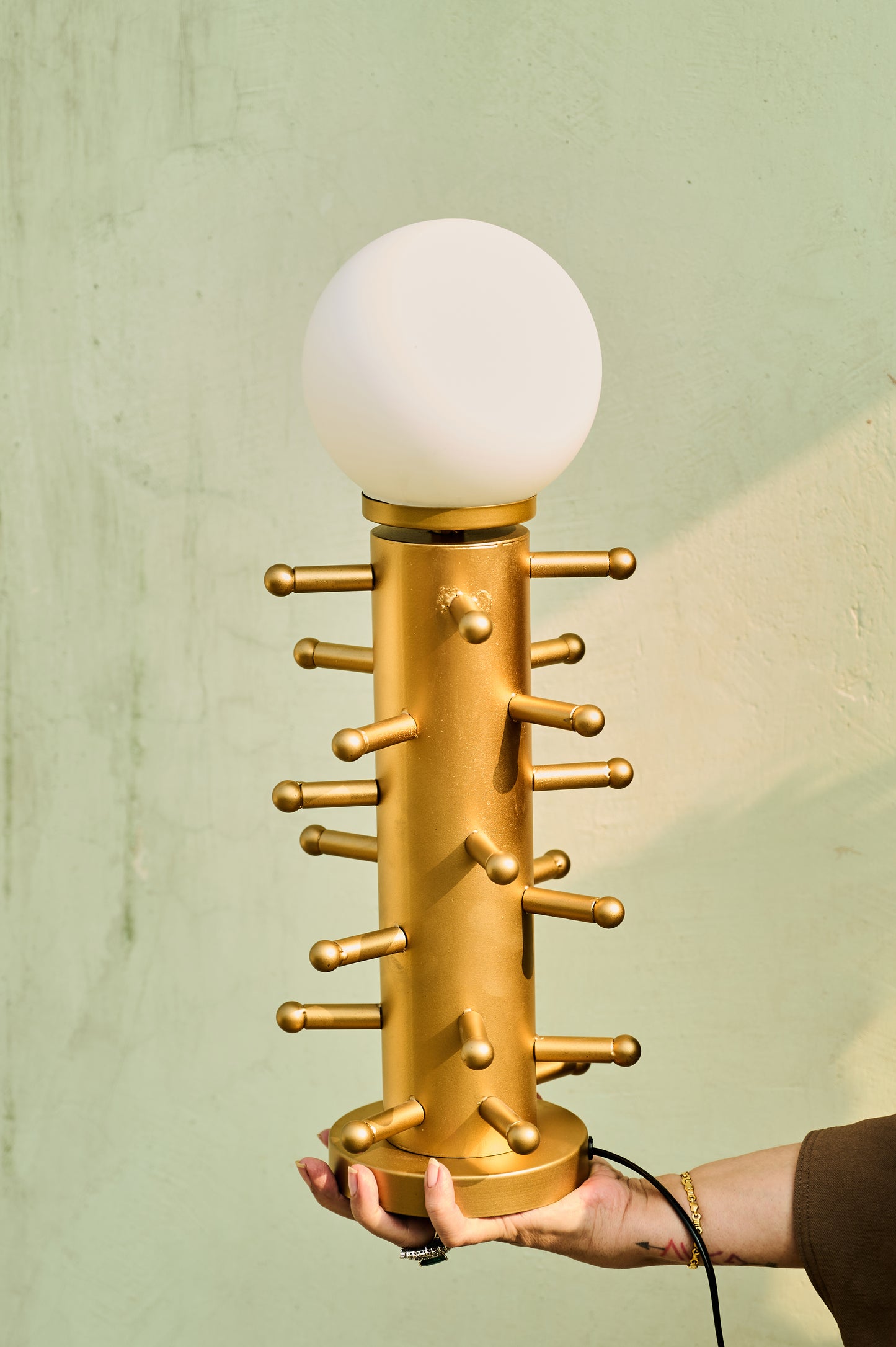 Gold table lamp with a white bulb held by a person against a green background