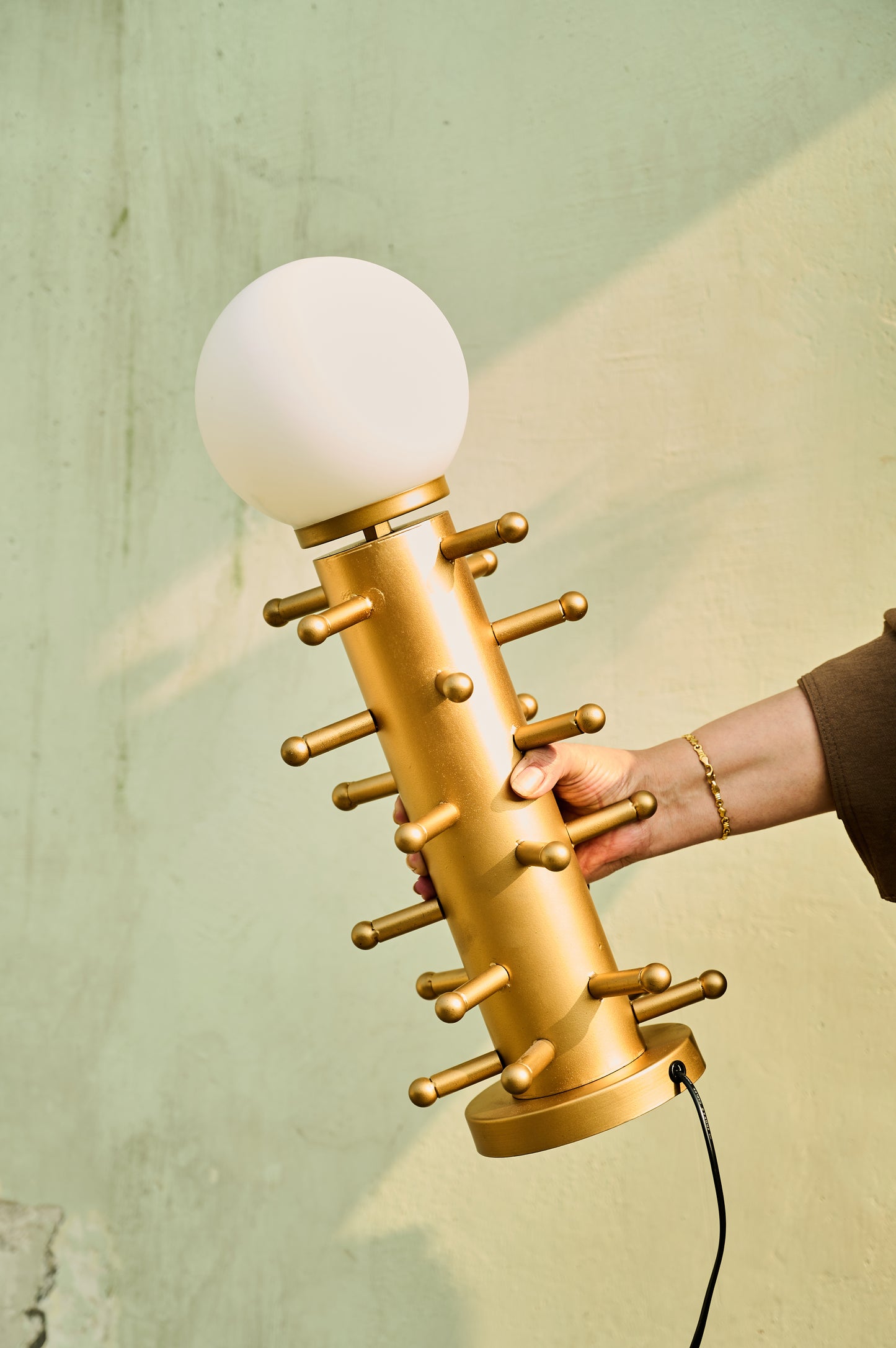 Gold massage gun held by a hand against a light green background