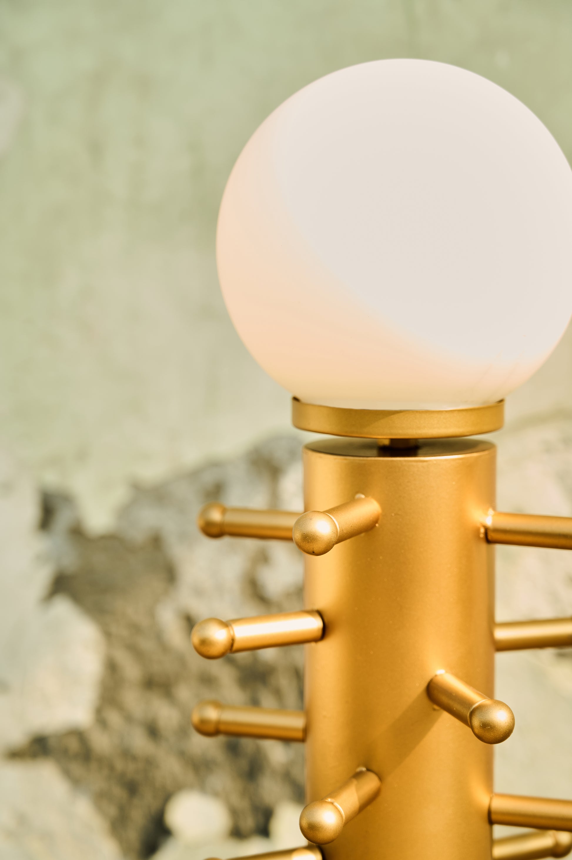 Gold lamp with a white globe shade against a textured wall.