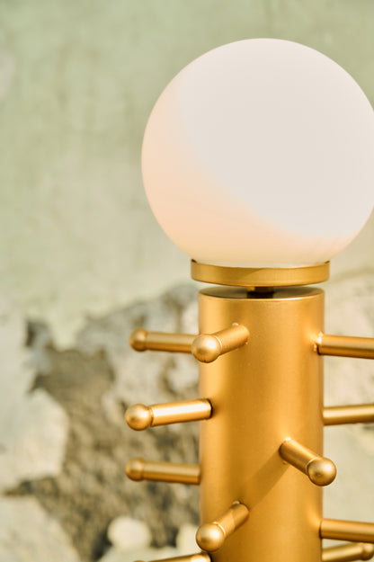 Gold lamp with a white globe shade against a textured wall.