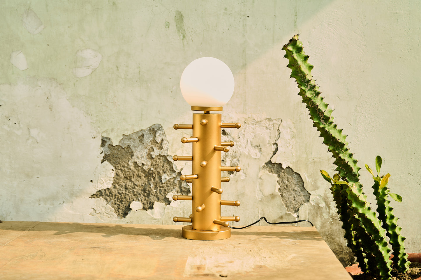 Gold table lamp with a white bulb on a wooden surface against a textured wall.