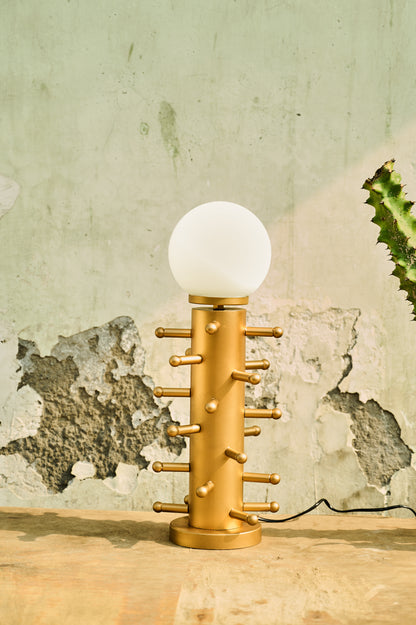 Gold lamp with a white bulb on a wooden surface against a textured wall.