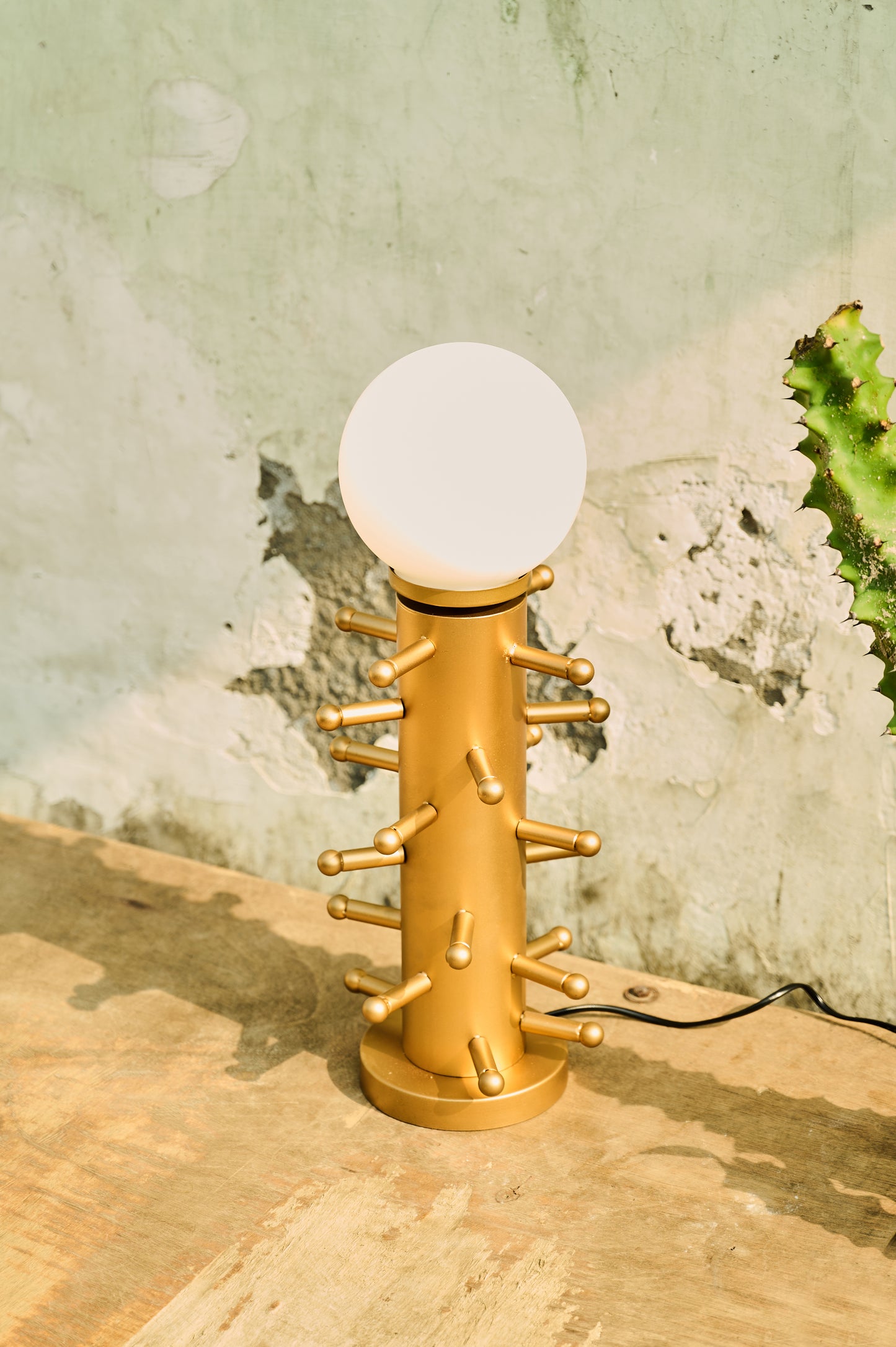 Gold lamp with a white bulb on a wooden surface against a textured wall.