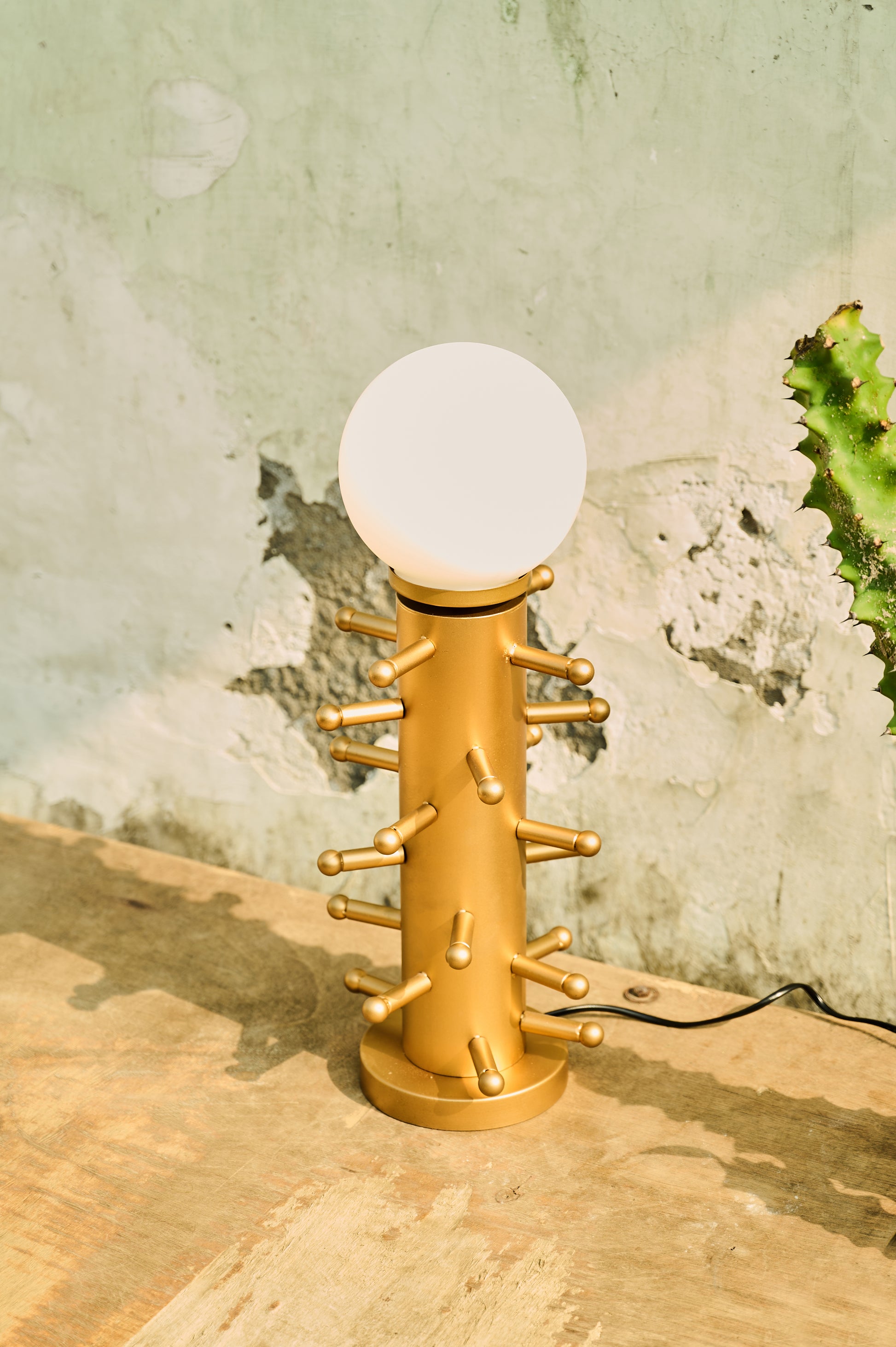 Gold lamp with a white bulb on a wooden surface against a textured wall.